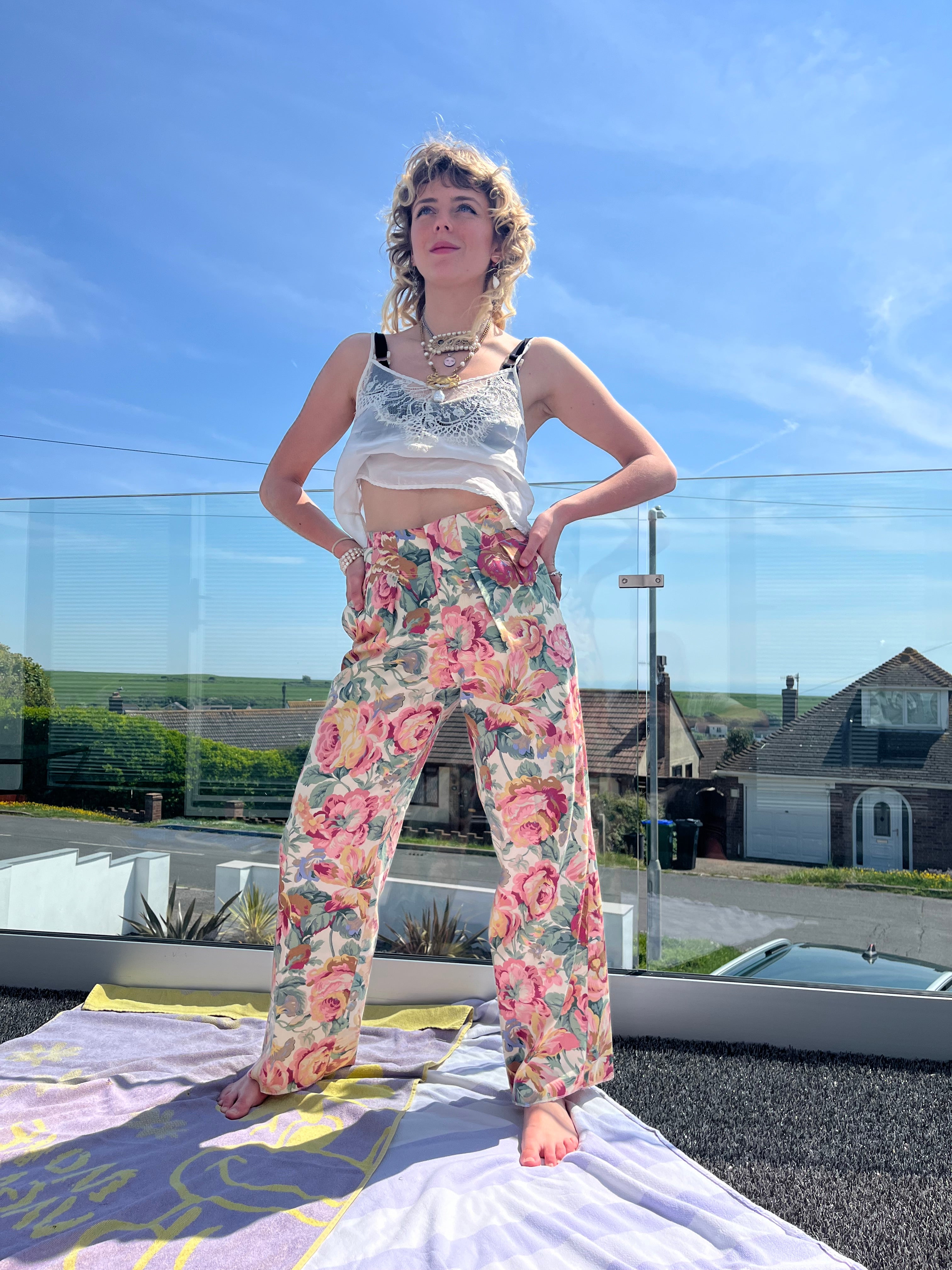 Person wearing a floral outfit standing in front of a reflective surface with a house and car in the background.