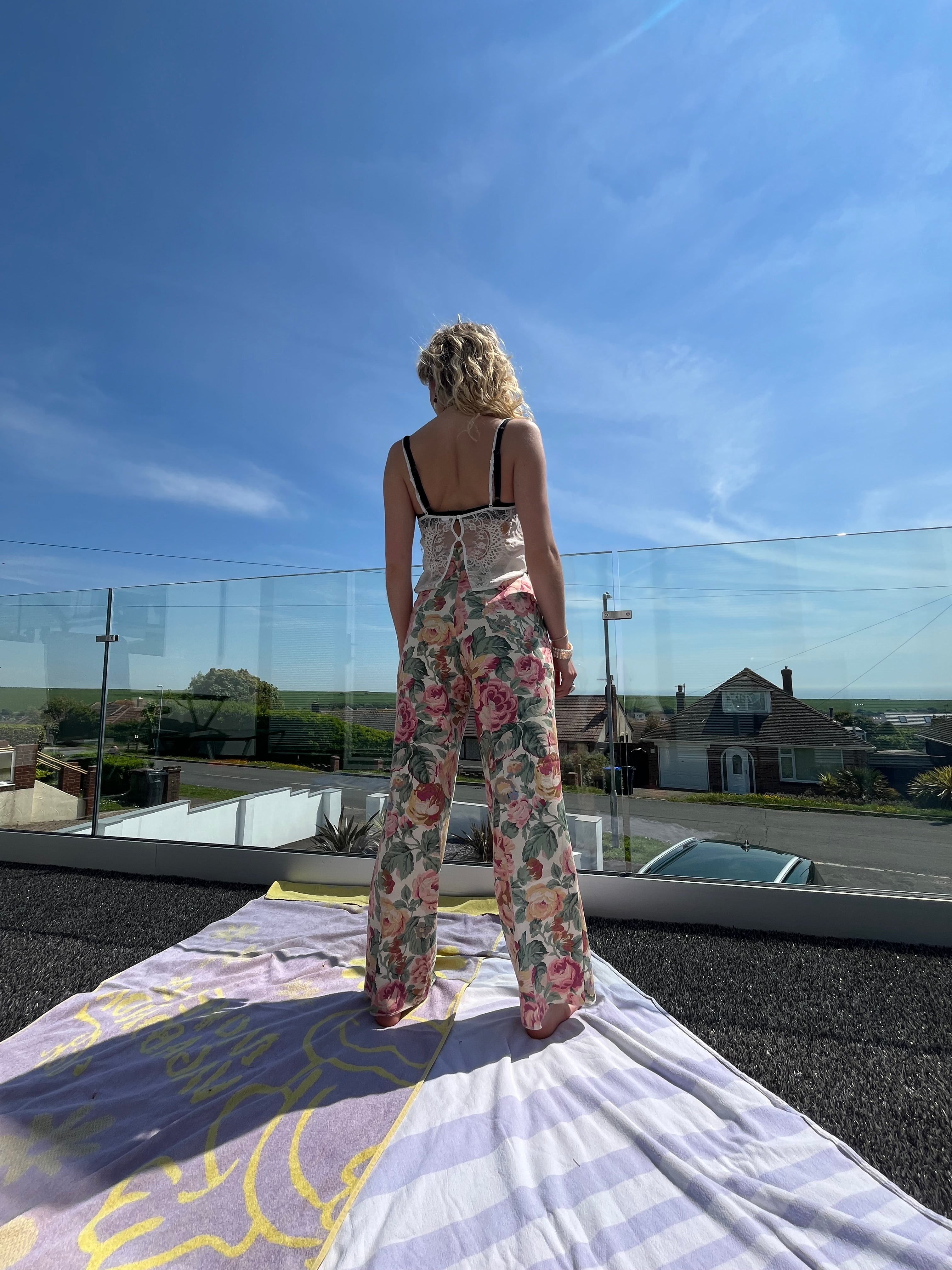 Person wearing a floral dress standing on a dock with a clear blue sky and water in the background.