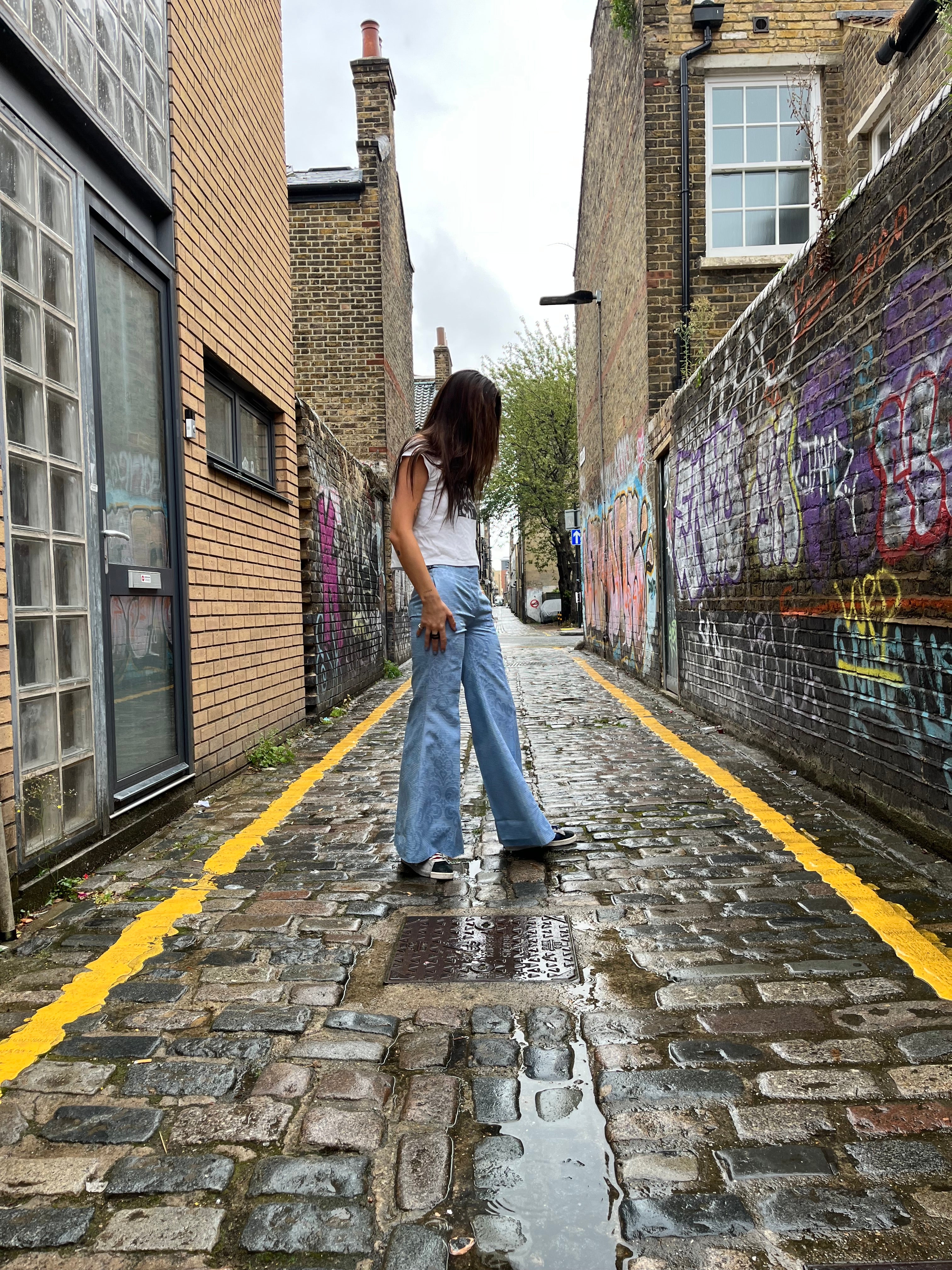 Person sitting on a stone wall with graffiti above, looking at a phone.