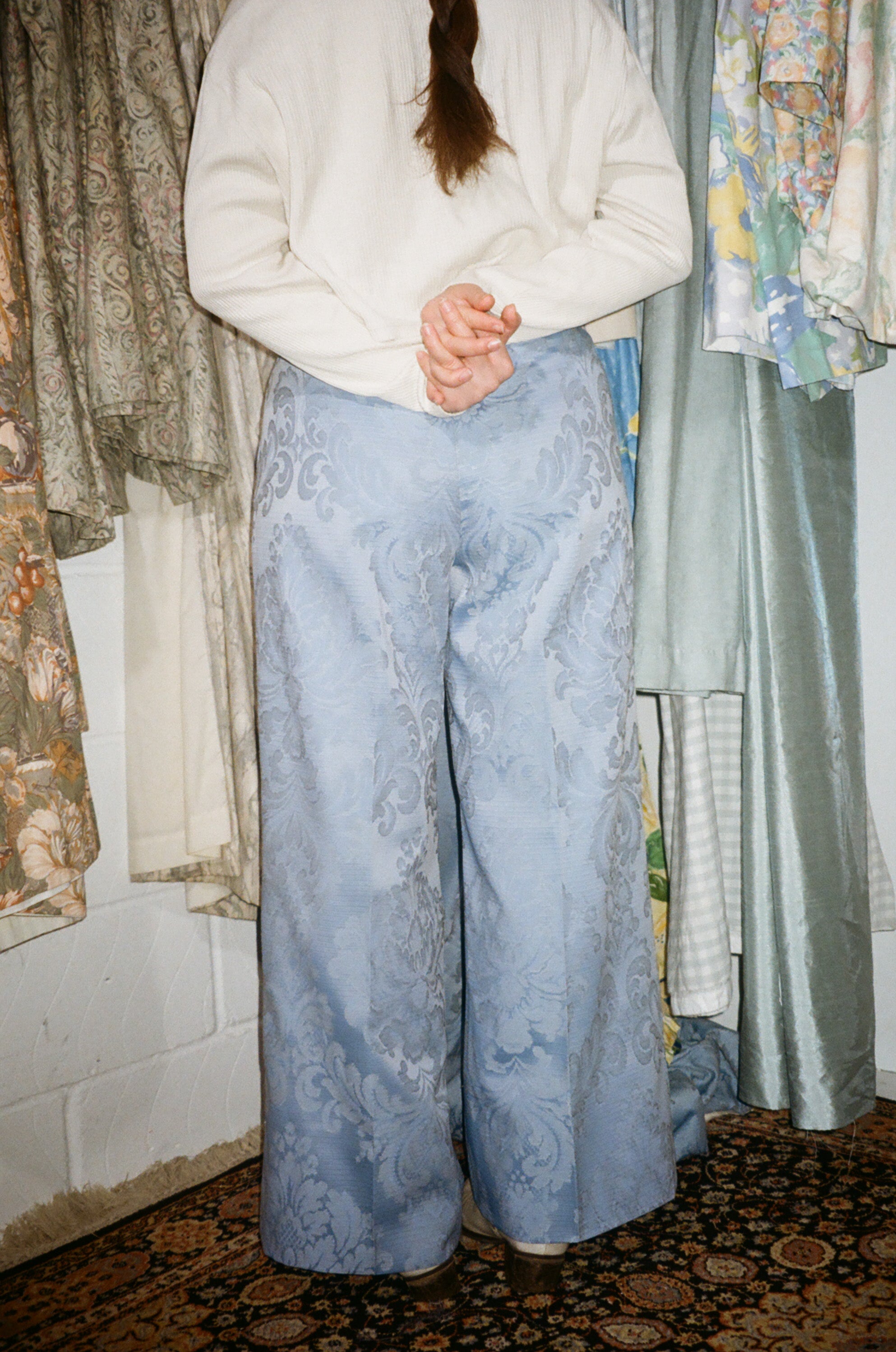 Person wearing light blue patterned pants standing in front of a curtain with floral patterns.