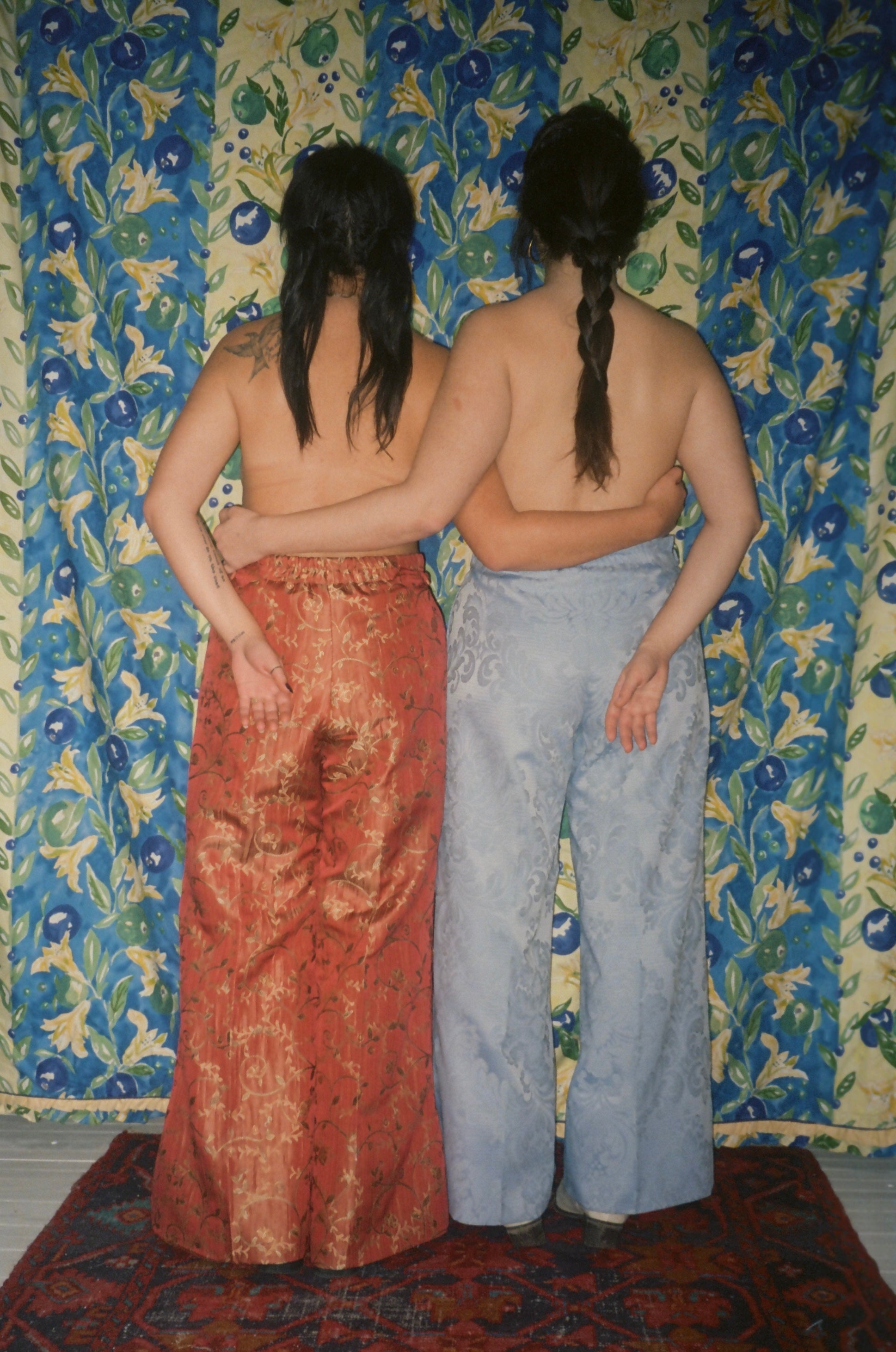 Two people standing back-to-back against a floral-patterned wall.