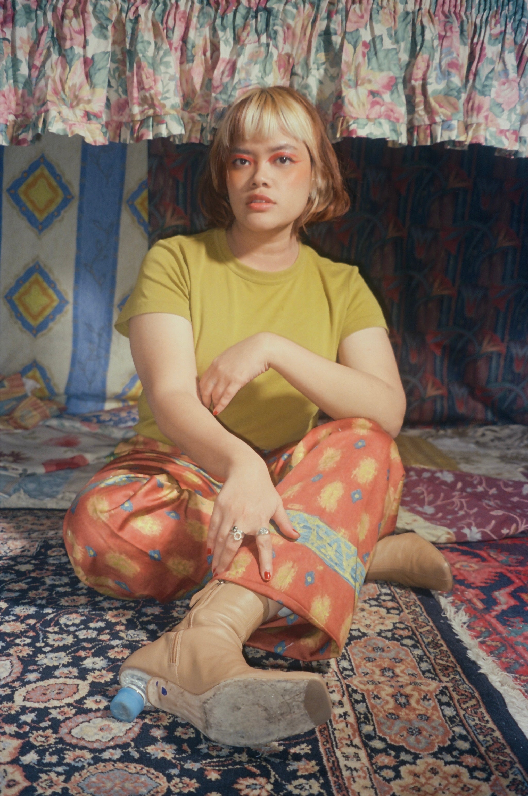 Person sitting on a patterned rug wearing a yellow shirt and colorful pants.