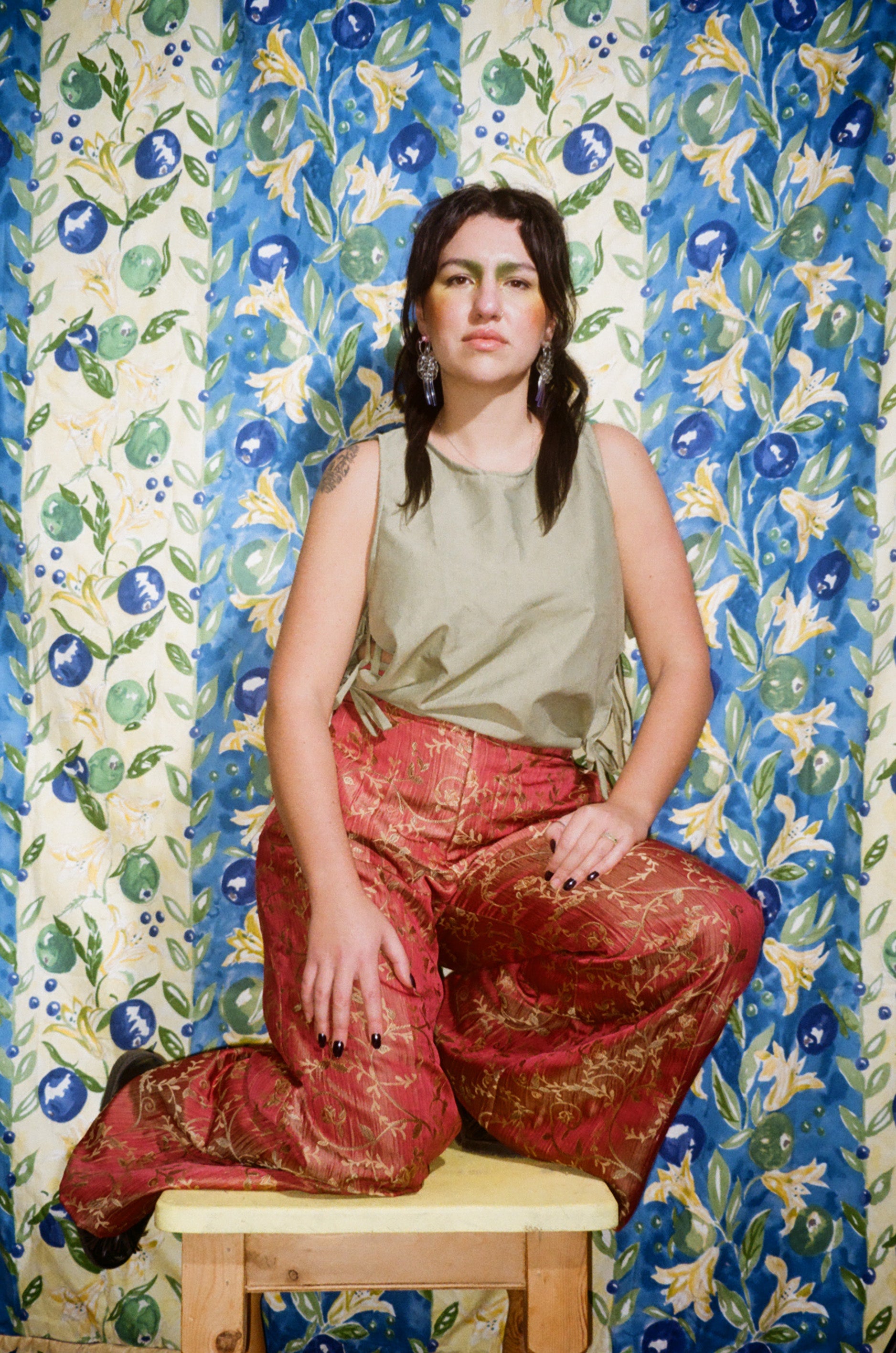 Woman sitting on a stool against a colorful floral-patterned wall.