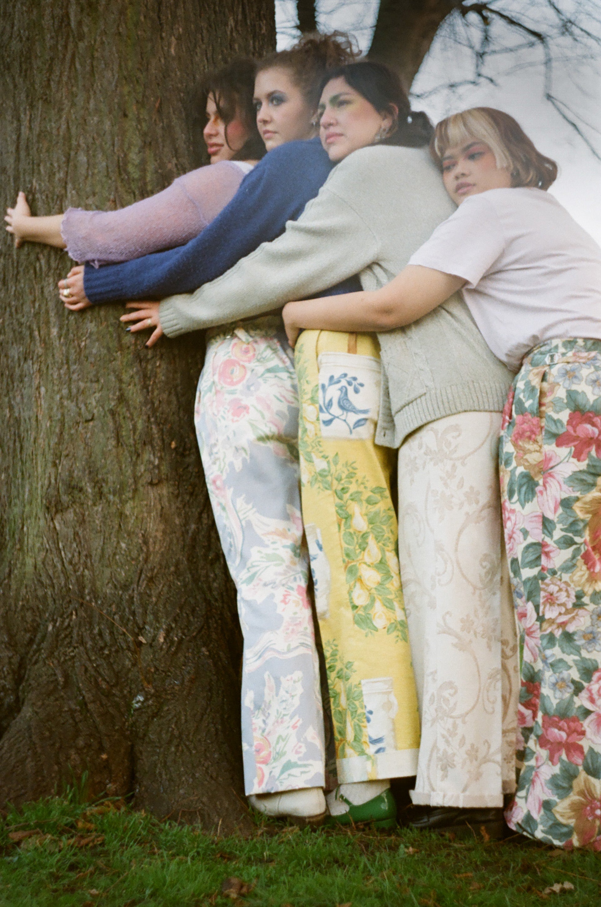 Four women hugging a tree, wearing patterned pants.