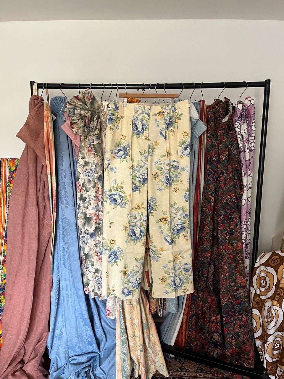 Collection of floral and solid-colored dresses hanging on a rack against a white wall.